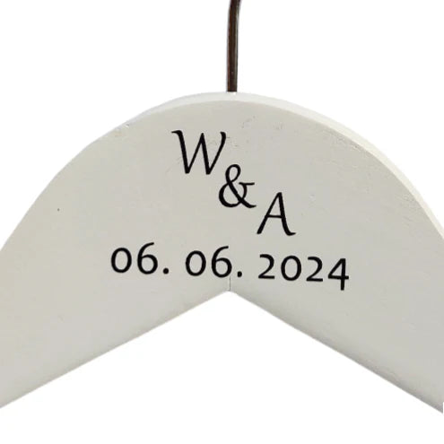 close-up van witte houten kledinghanger met initialen en trouwdatum. 